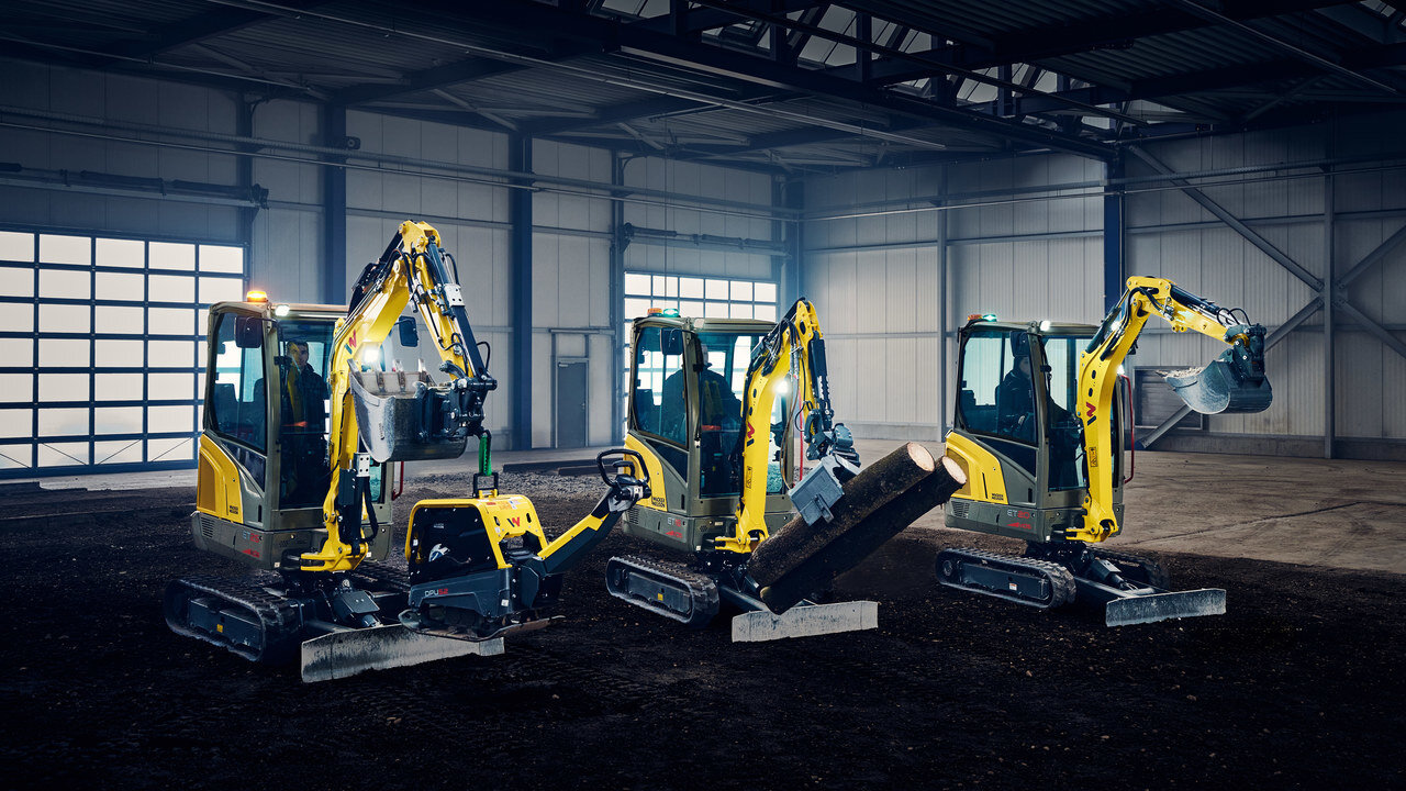 three yellow mini excavators standing in an industry hall and carrying heavy equipemnt