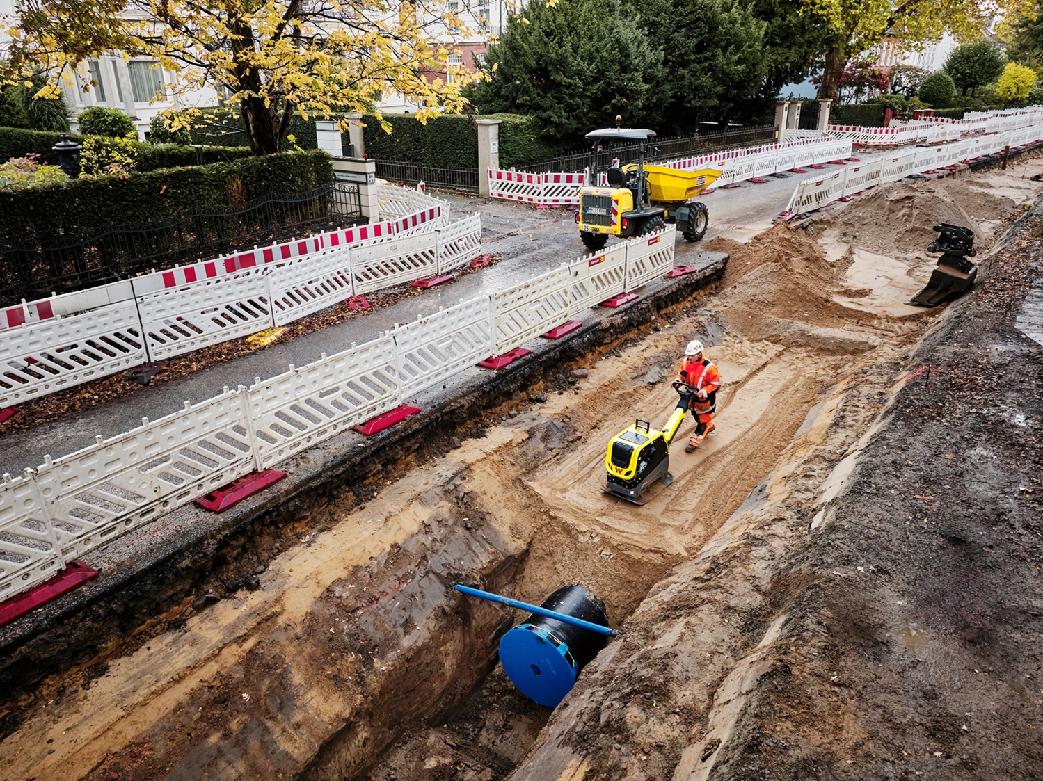 Strabag Bauarbeiter verdichtet Baugrube mit Wacker Neuson Vibrationsplatte auf urbaner Baustelle