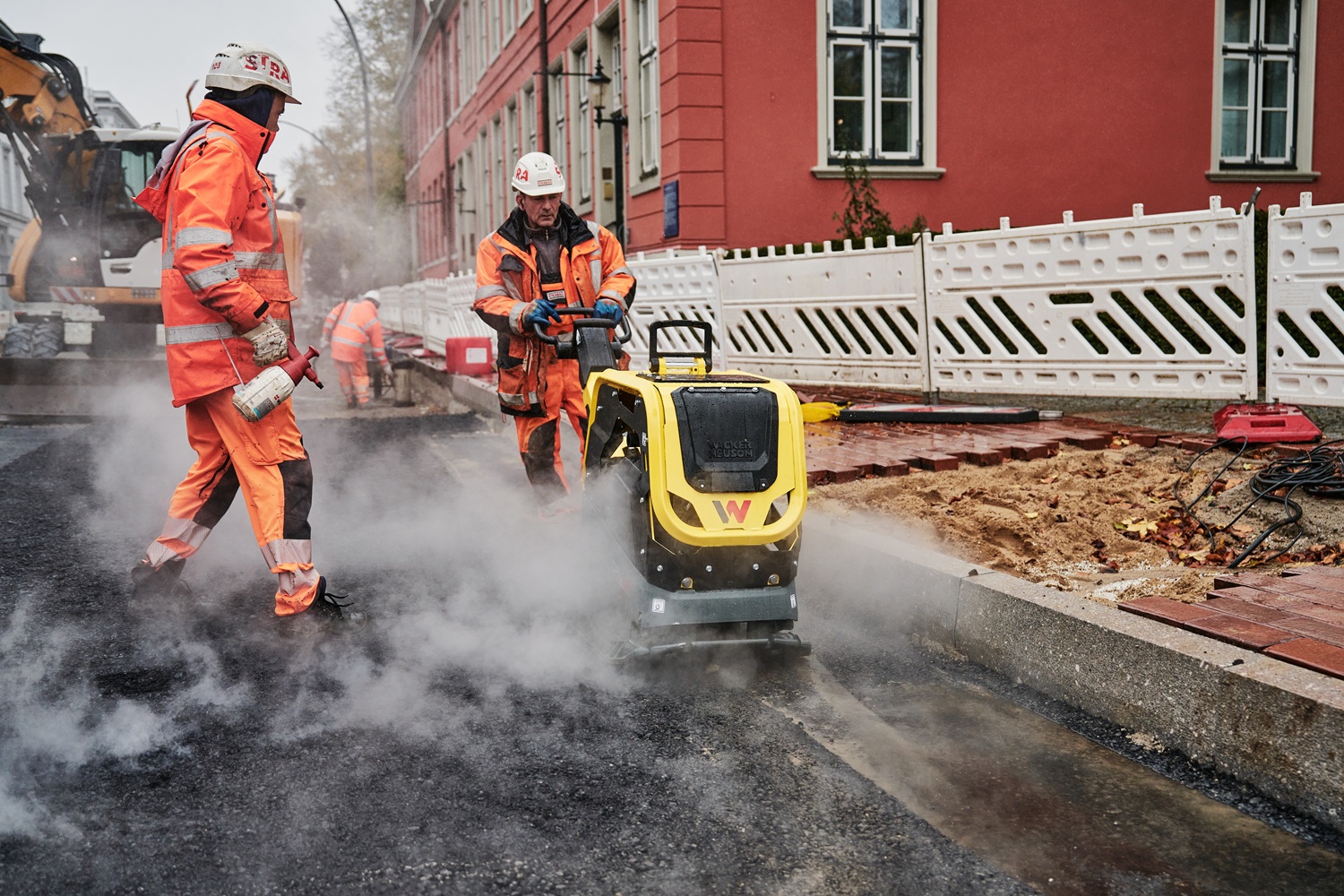 Strabag Bauarbeiter verdichtet Asphalt mit Wacker Neuson Vibrationsplatte auf emissionsarmer Baustelle